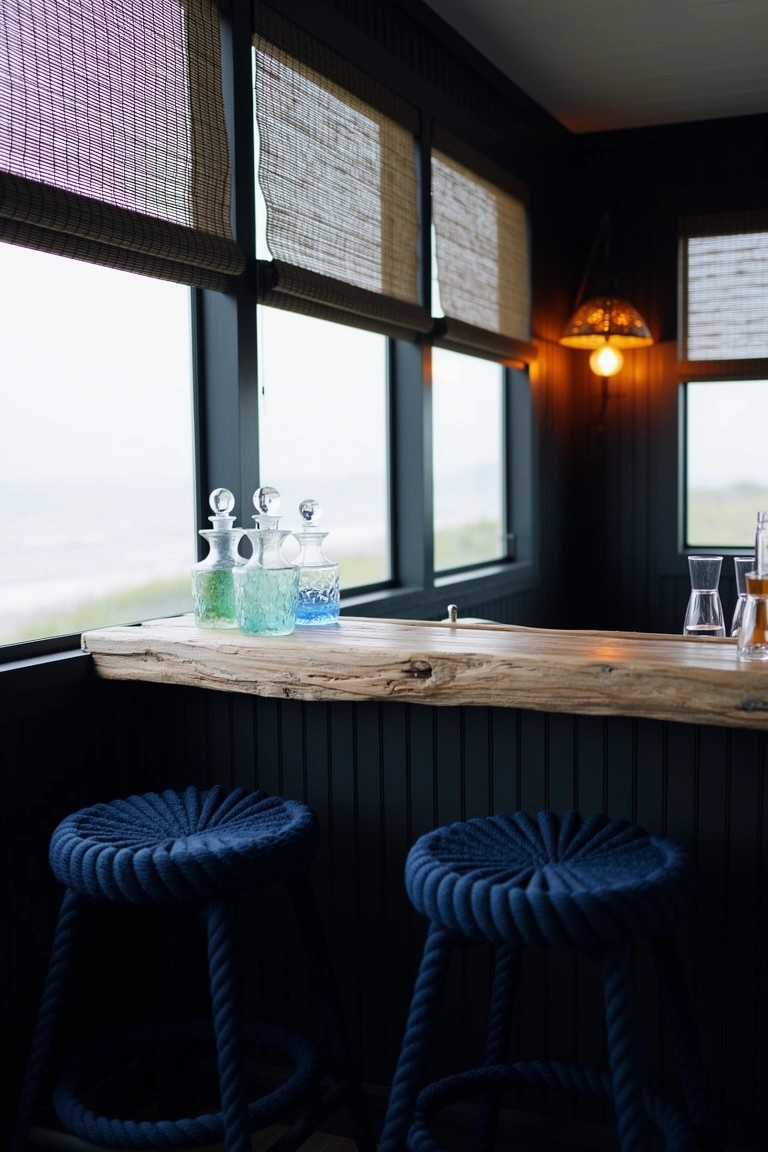 Rustic live-edge wood bar counter with navy rope stools in a dark paneled speakeasy nook, glass bottles, and bamboo shades on windows