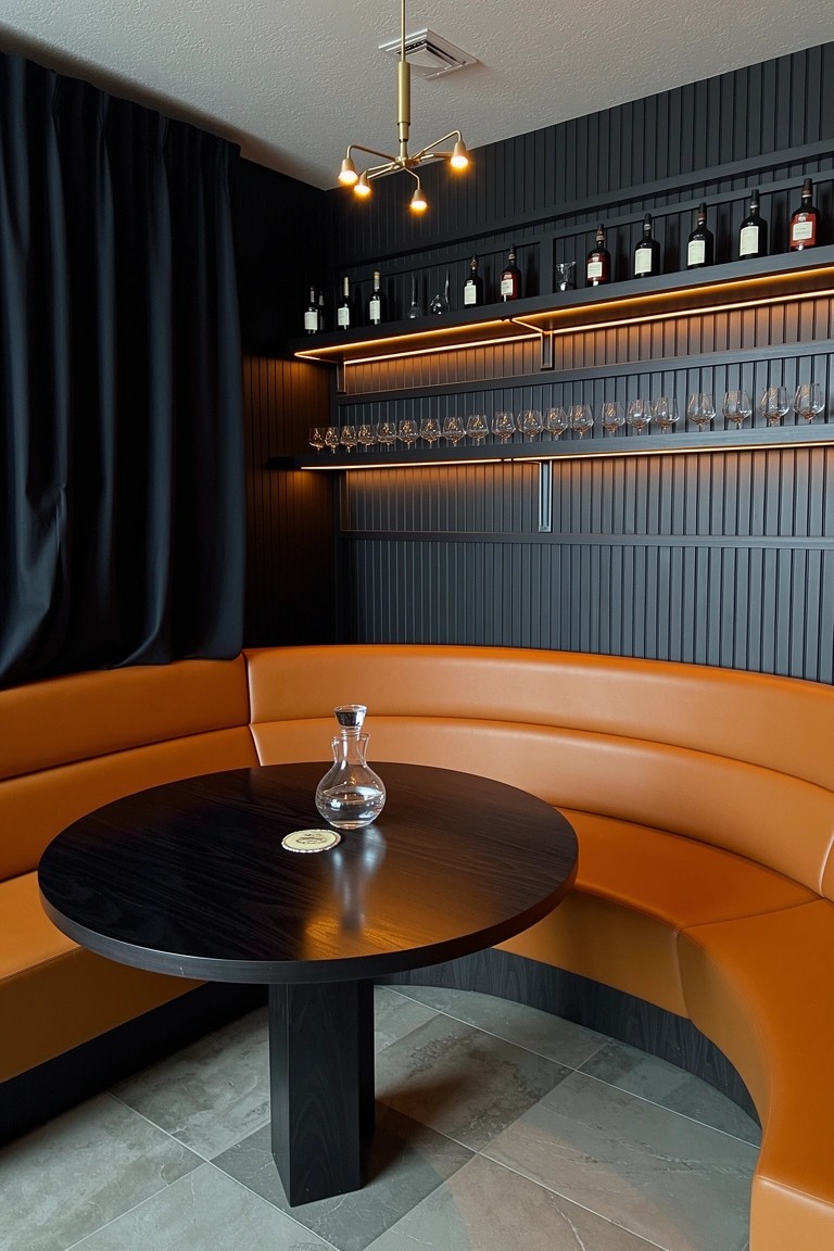 Curved orange leather booth in a dark-paneled corner with black table and wine shelves