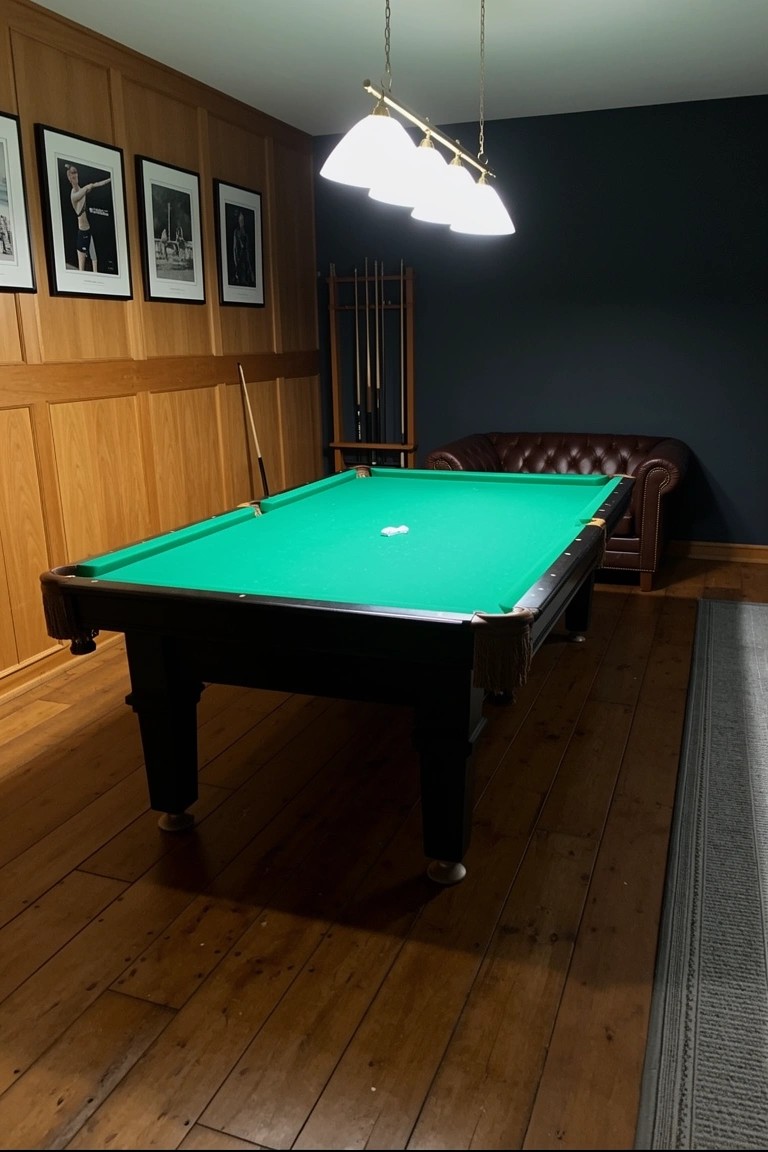 Wood-paneled room with central green billiards table, leather armchair, and cue rack