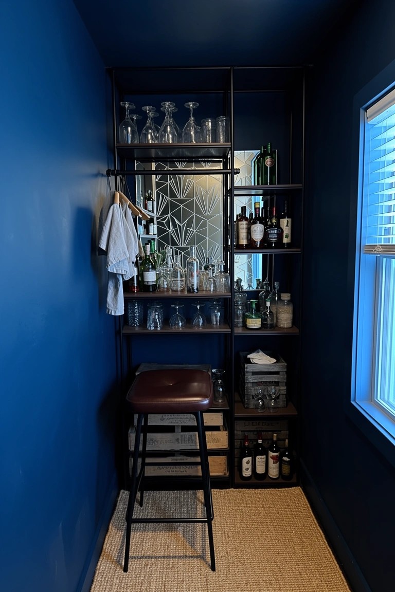 Compact deep blue speakeasy bar nook with black metal open shelving stocked with liquor bottles and glassware, plus a bar stool