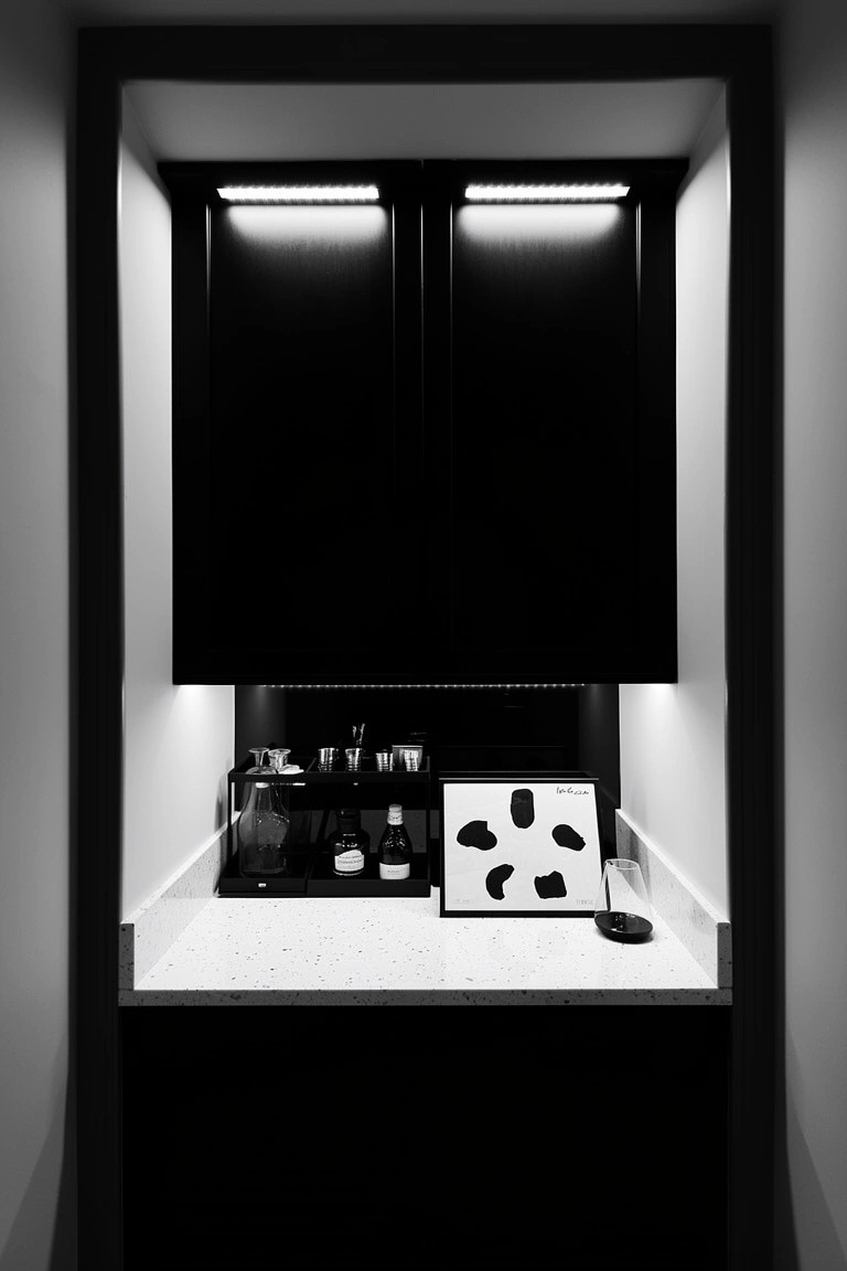 Recessed black cabinet bar nook with LED lights, coffee station, and abstract art on white counter