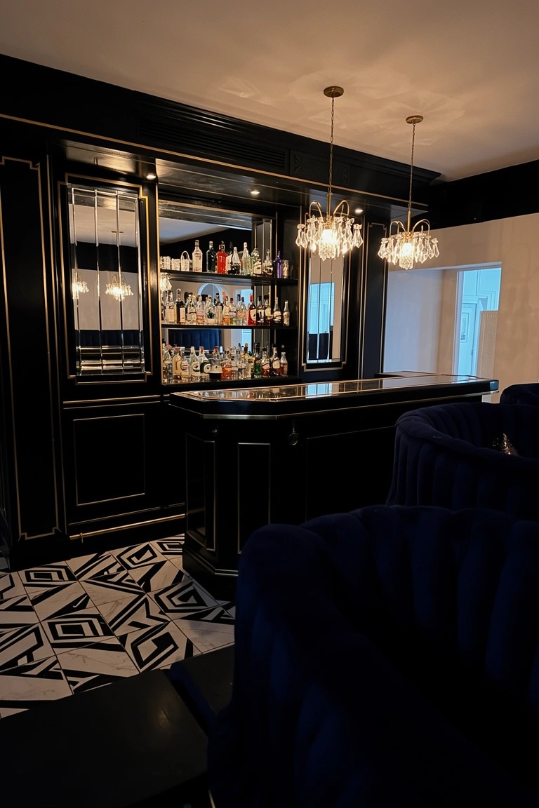 Black lacquered bar cabinets with mirrored shelves full of liquor bottles, gold accents, blue velvet stools, and geometric black and white floor in a basement speakeasy