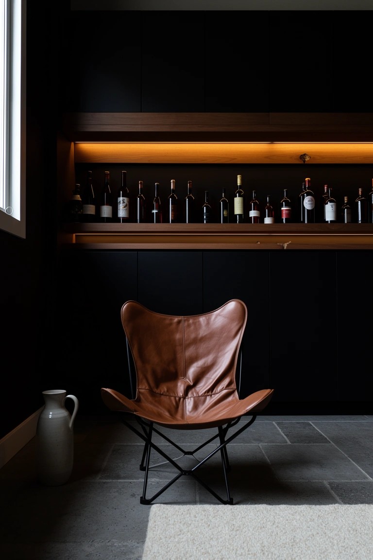 Tan leather sling chair facing a backlit wooden shelf of whiskey bottles in a dark cabinet-lined room