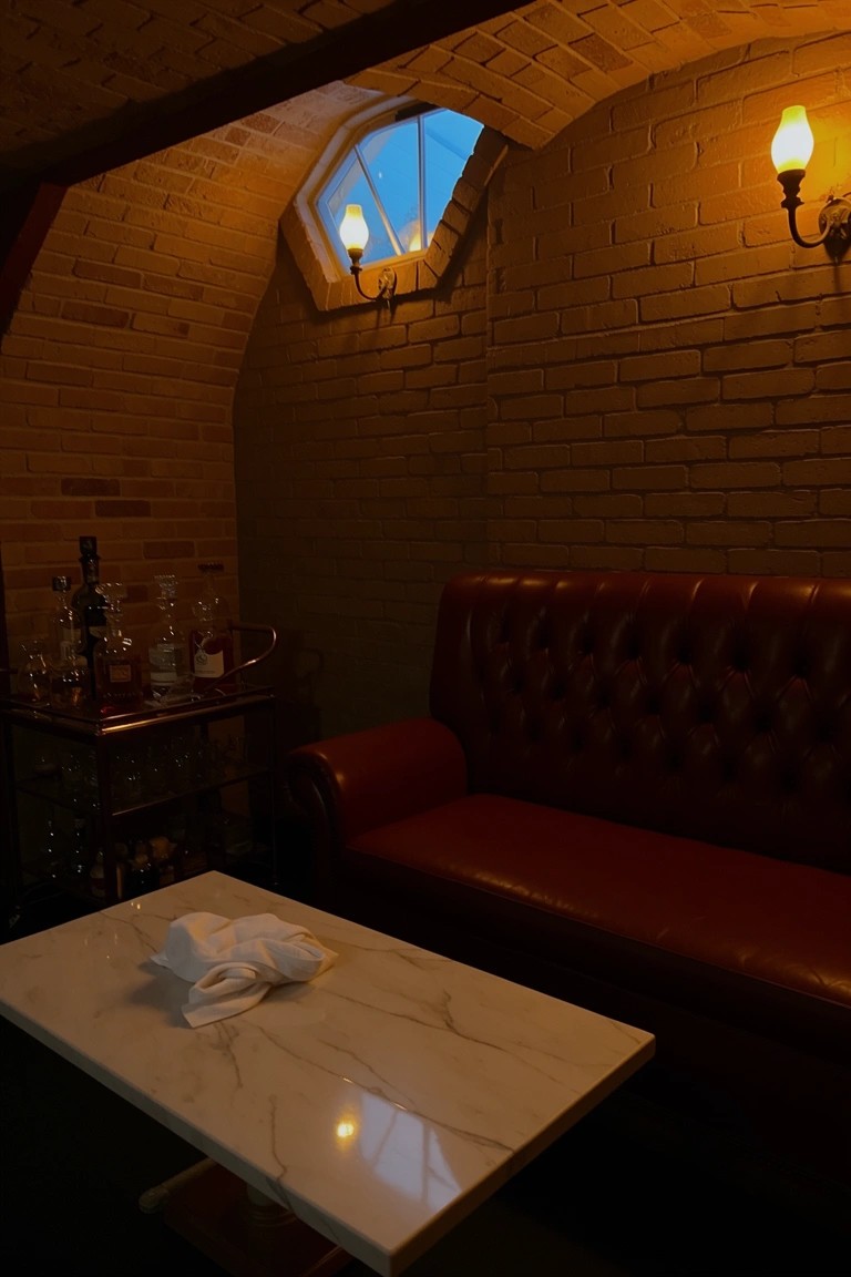 Cozy vaulted brick room with red tufted leather sofa, marble table, and bar cart under warm wall lights