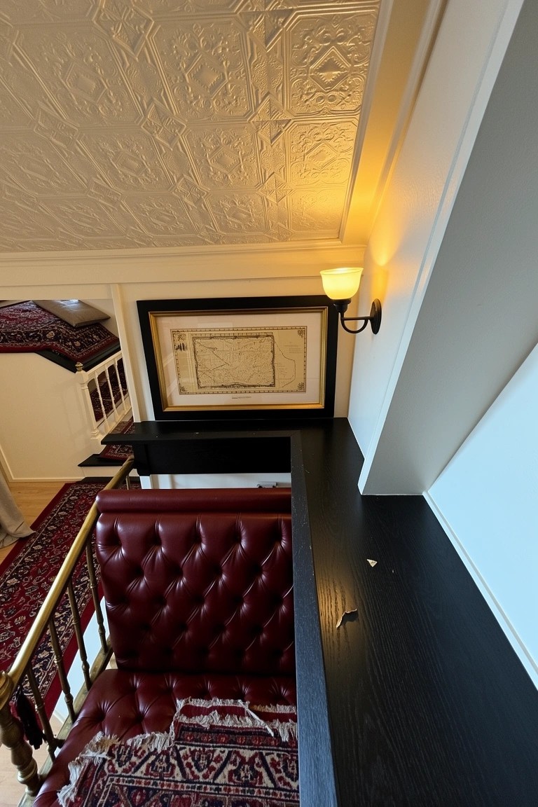 Overhead view of a vintage balcony home bar with red leather tufted banquette along brass railing, black wood shelf, and framed artwork