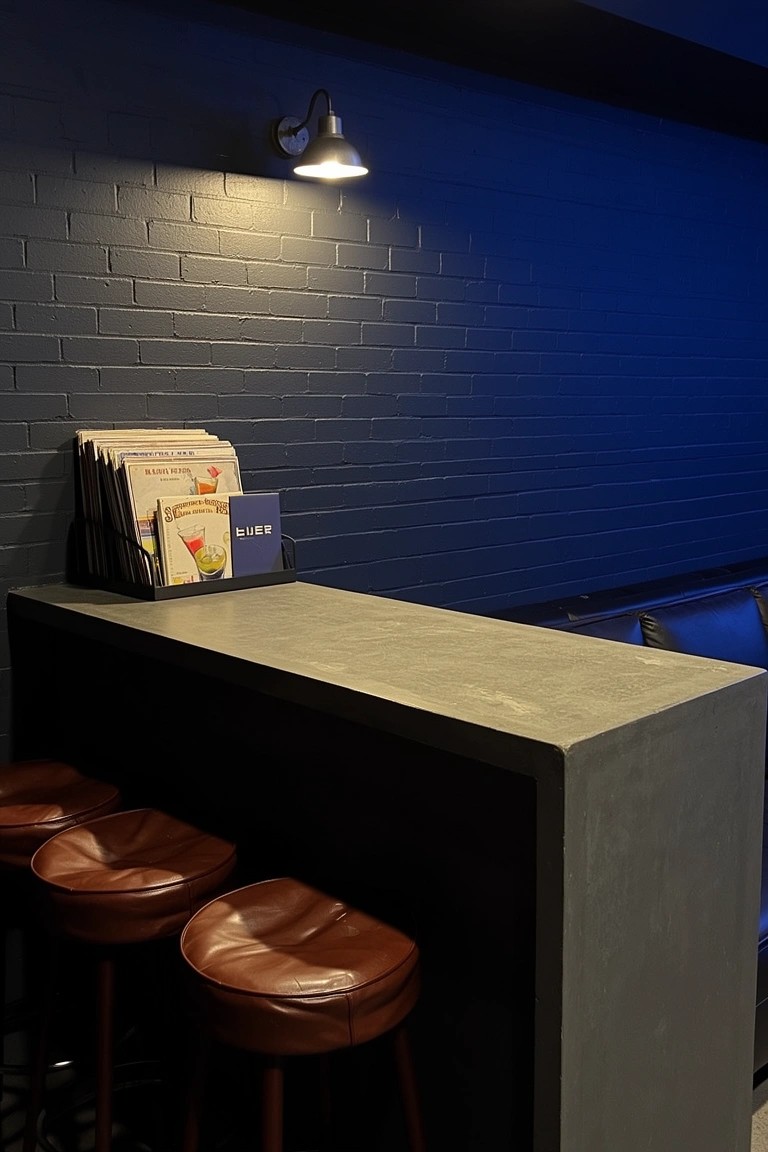 Dark brick wall behind concrete home bar counter with leather barstools and wall lamp