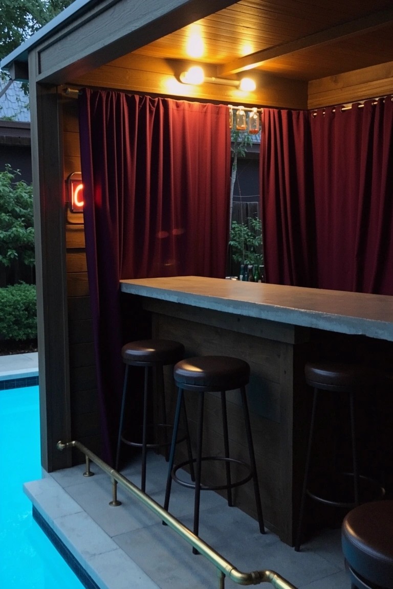 Outdoor pergola bar enclosed by maroon curtains with neon sign, concrete countertop, leather stools, and pool nearby