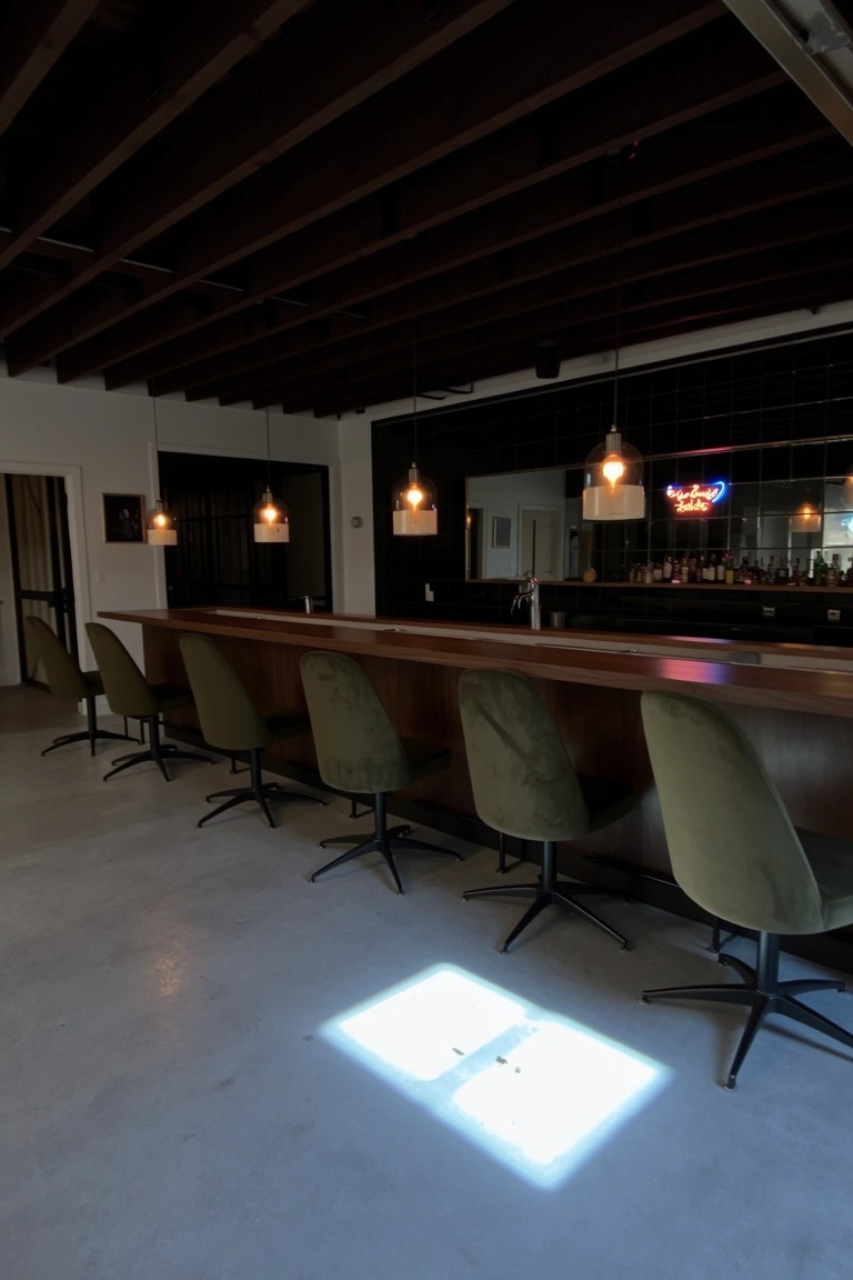 Row of green velvet swivel bar stools lining a light wood bar counter in a moody industrial space with exposed ceiling beams
