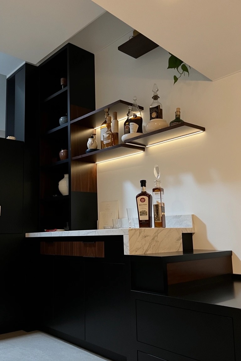 Modern black bar cabinetry with backlit floating shelves holding whiskey bottles and glassware