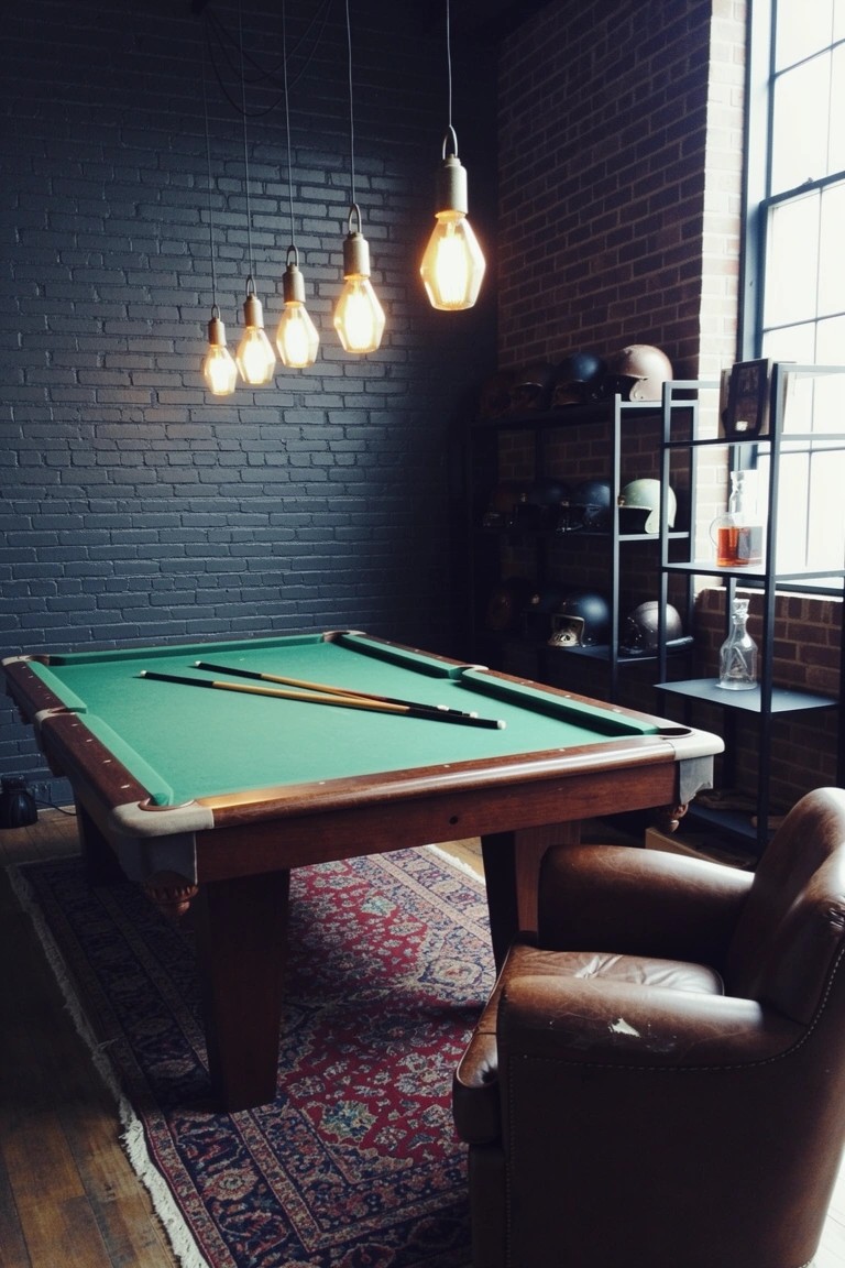 Moody man cave with green pool table against dark exposed brick wall, industrial pendant lights overhead, leather armchair nearby