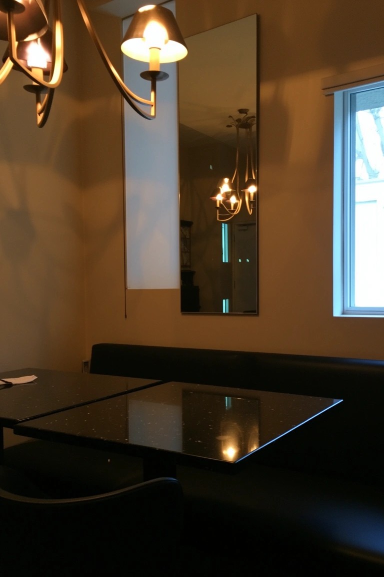 Small speakeasy lounge with black leather booth seating, glossy black tables, tall mirror on wall, and warm chandelier lights