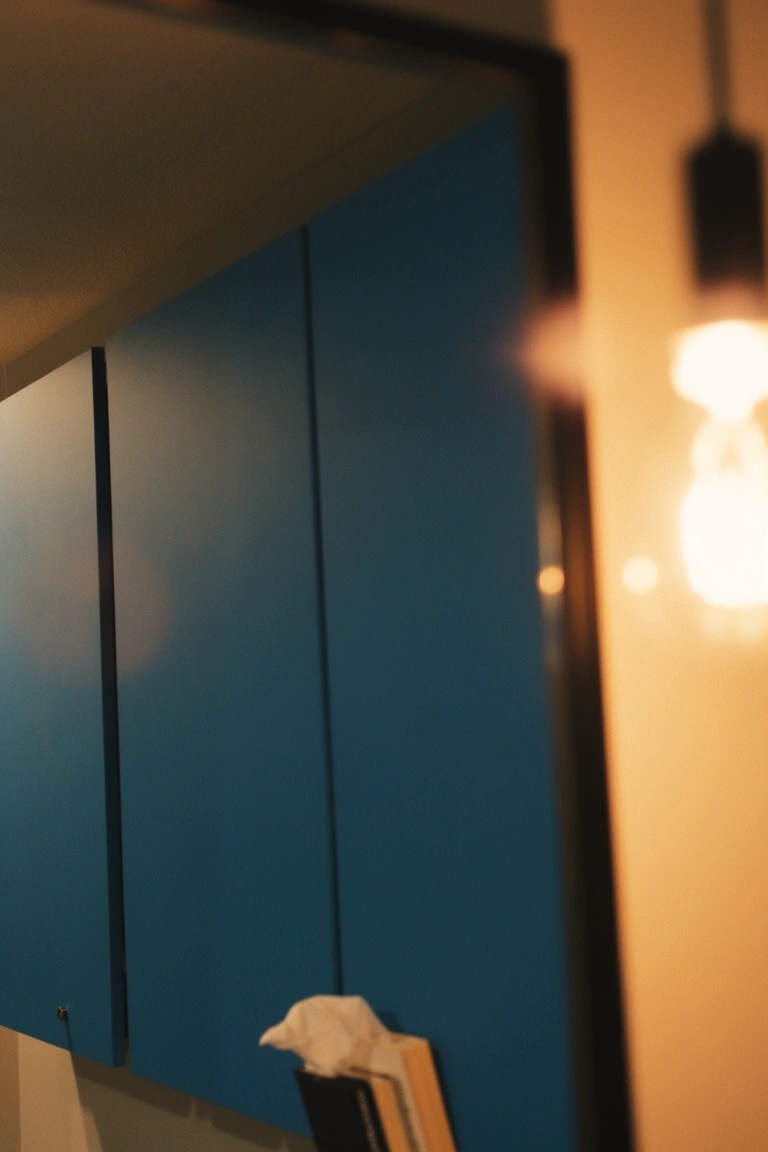 Navy blue cabinets reflected in a black-framed mirror above a vanity with books, tissue box, and warm pendant lamp