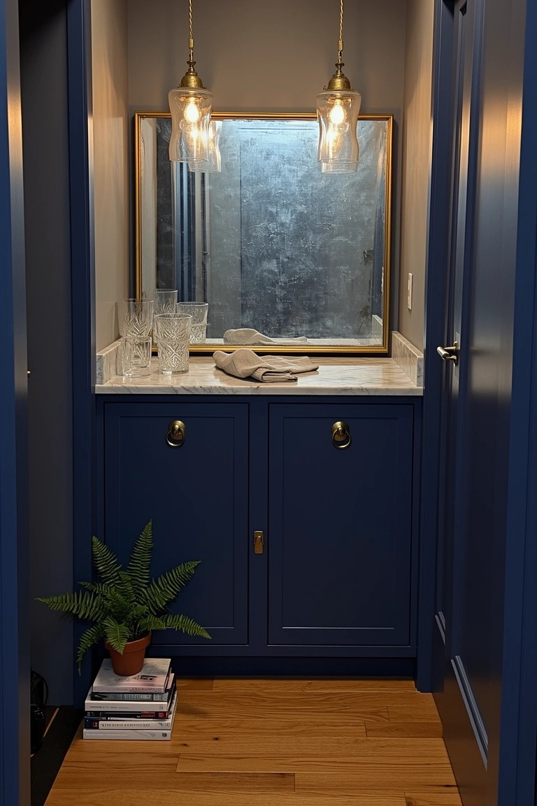 Compact powder room vanity with deep navy cabinets, white marble countertop, brass pendant lights, and round mirror