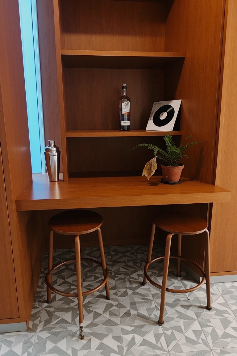 Compact built-in wooden bar nook with shelves for bottles and shaker, wooden stools, potted plant, and geometric tile floor