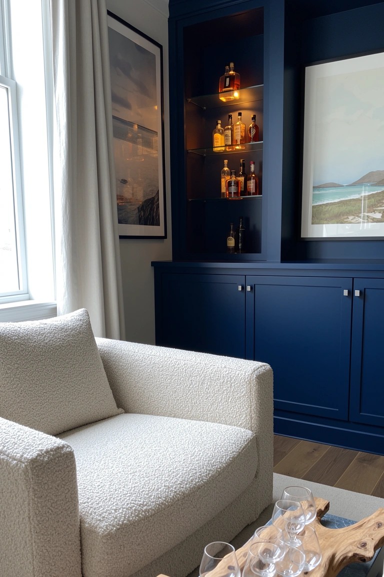 Navy blue built-in cabinet with internal lighting displaying whiskey bottles next to a white armchair