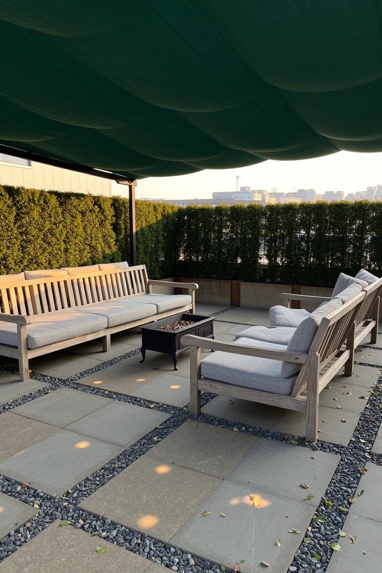 Wooden benches with neutral cushions arranged around a fire pit on a shaded terrace, edged by hedges