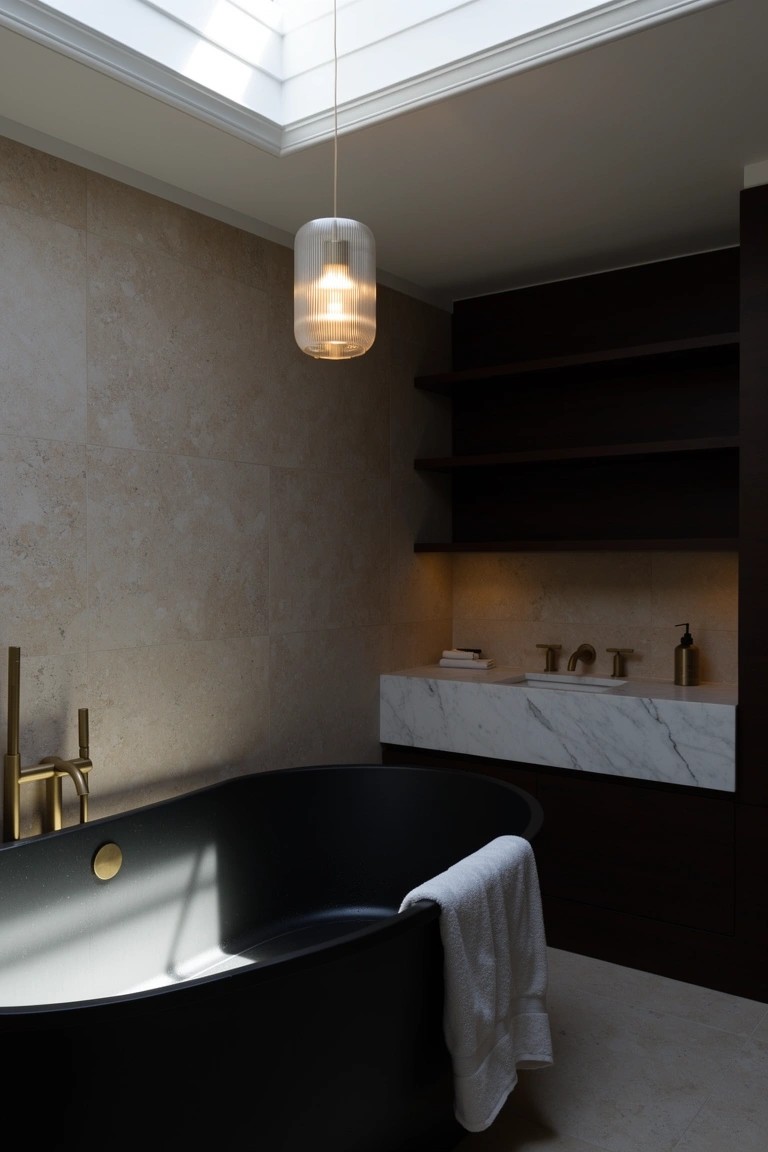 Sophisticated bathroom with matte black freestanding bathtub centered under skylight, neutral stone walls, dark wood cabinets, white marble vanity and brass fixtures