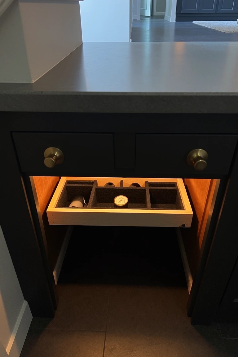 Base cabinet with pull-out divided tray for whiskey bottles, lit from below with gold hardware