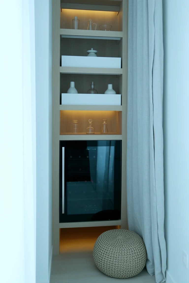 Tall narrow wooden built-in shelving with whiskey cooler at base and warm underlighting