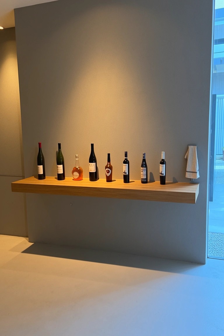 Minimalist floating oak shelf lined with whiskey and spirit bottles against a neutral gray wall