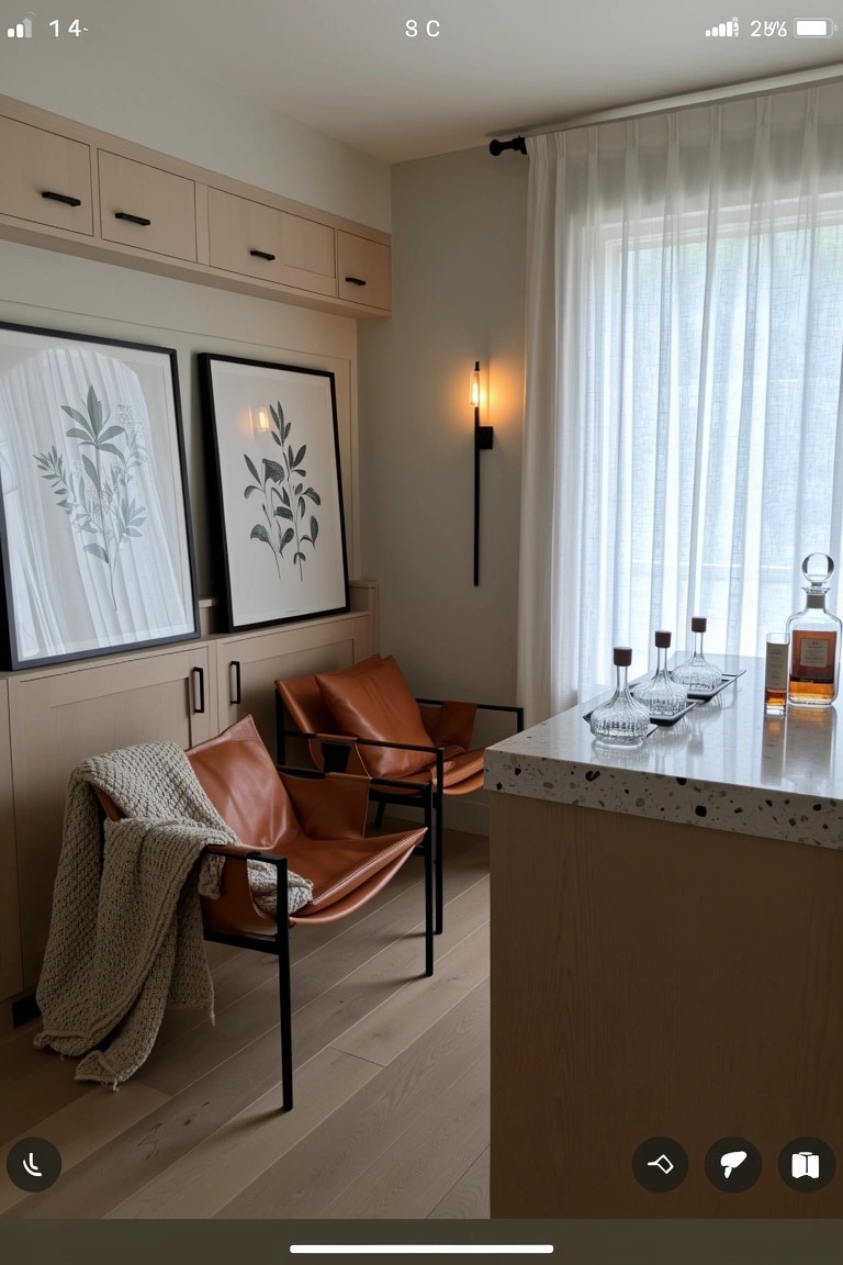 Two orange leather armchairs with a throw beside a speckled counter holding whiskey glasses and bottle in a neutral kitchen nook