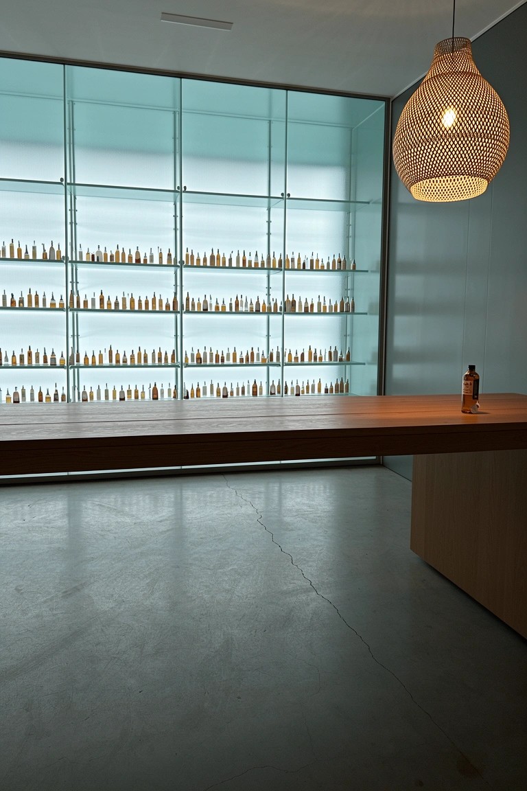 Modern whiskey bar with floor-to-ceiling glass shelves full of bottles behind a wooden counter