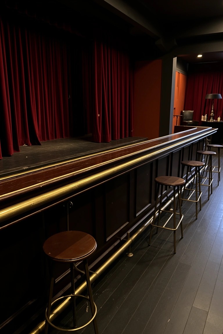 Basement speakeasy bar with polished wood counter and brass rails facing a small stage with red curtains