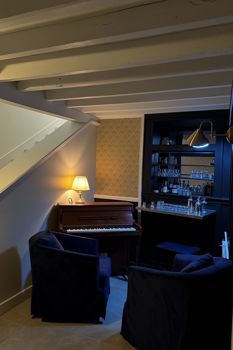 Compact basement piano bar nook with upright piano next to wooden bar shelves, blue armchairs, warm lamps, and exposed ceiling beams