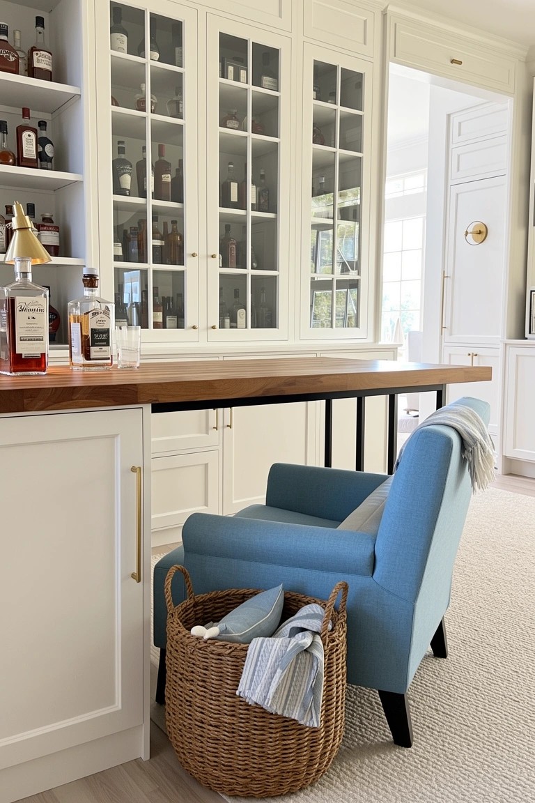 Glass-front white cabinets displaying whiskey bottles beside a wood bar top and blue armchair with wicker basket in a cozy home setup