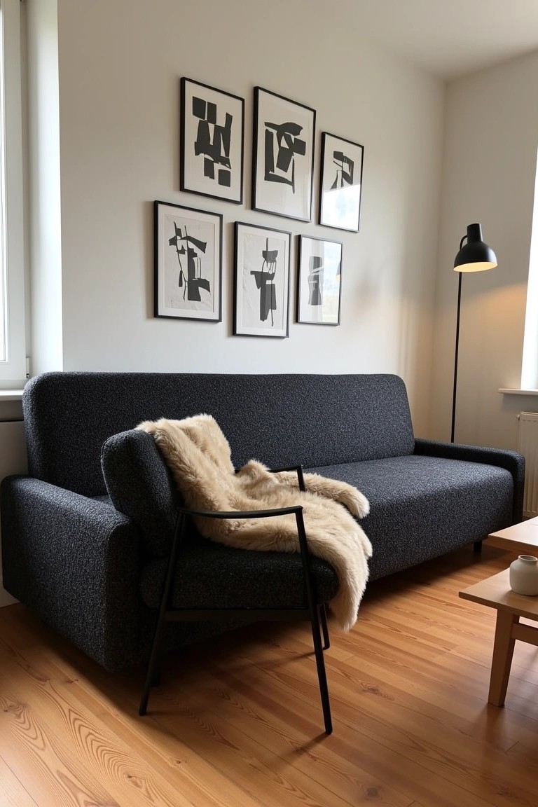 Masculine sitting room with grid of black and white abstract art above navy sofa draped in sheepskin throw, black chair, low wood table, and oak floors