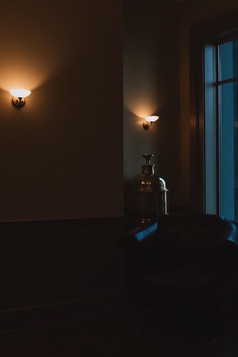 Room corner with paired wall sconces casting warm light on wood-paneled walls near a window