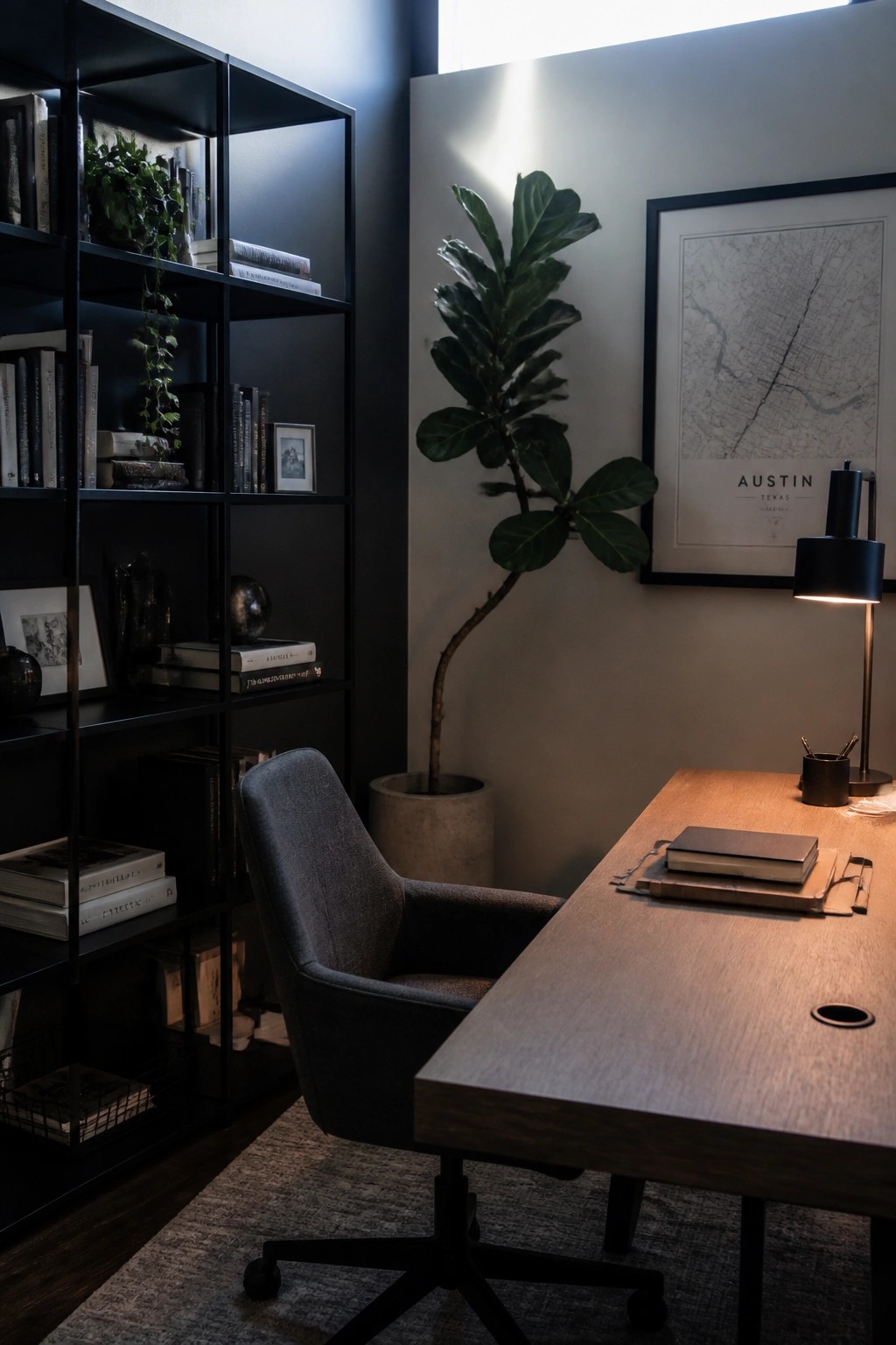 A home office with black shelving units, a wooden desk, gray chair, large potted plant, and framed map on the wall.