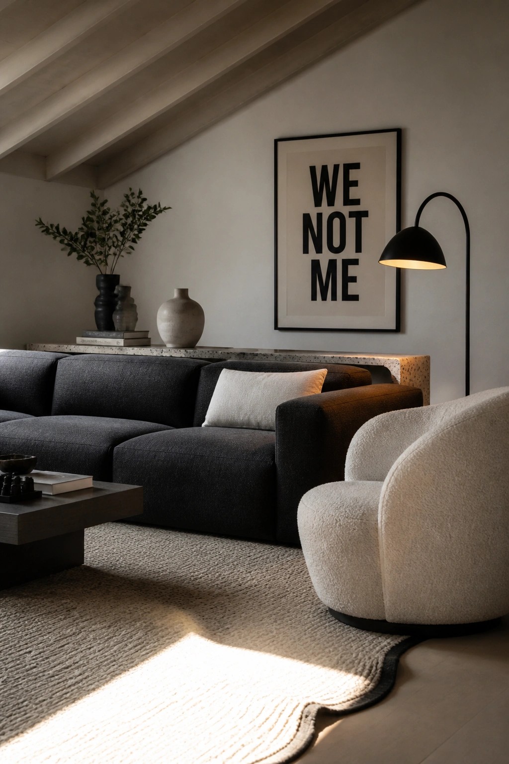 A living room featuring a large dark gray sectional sofa, a white bouclé swivel chair, a black floor lamp, and a framed black and white art print on a light wall.