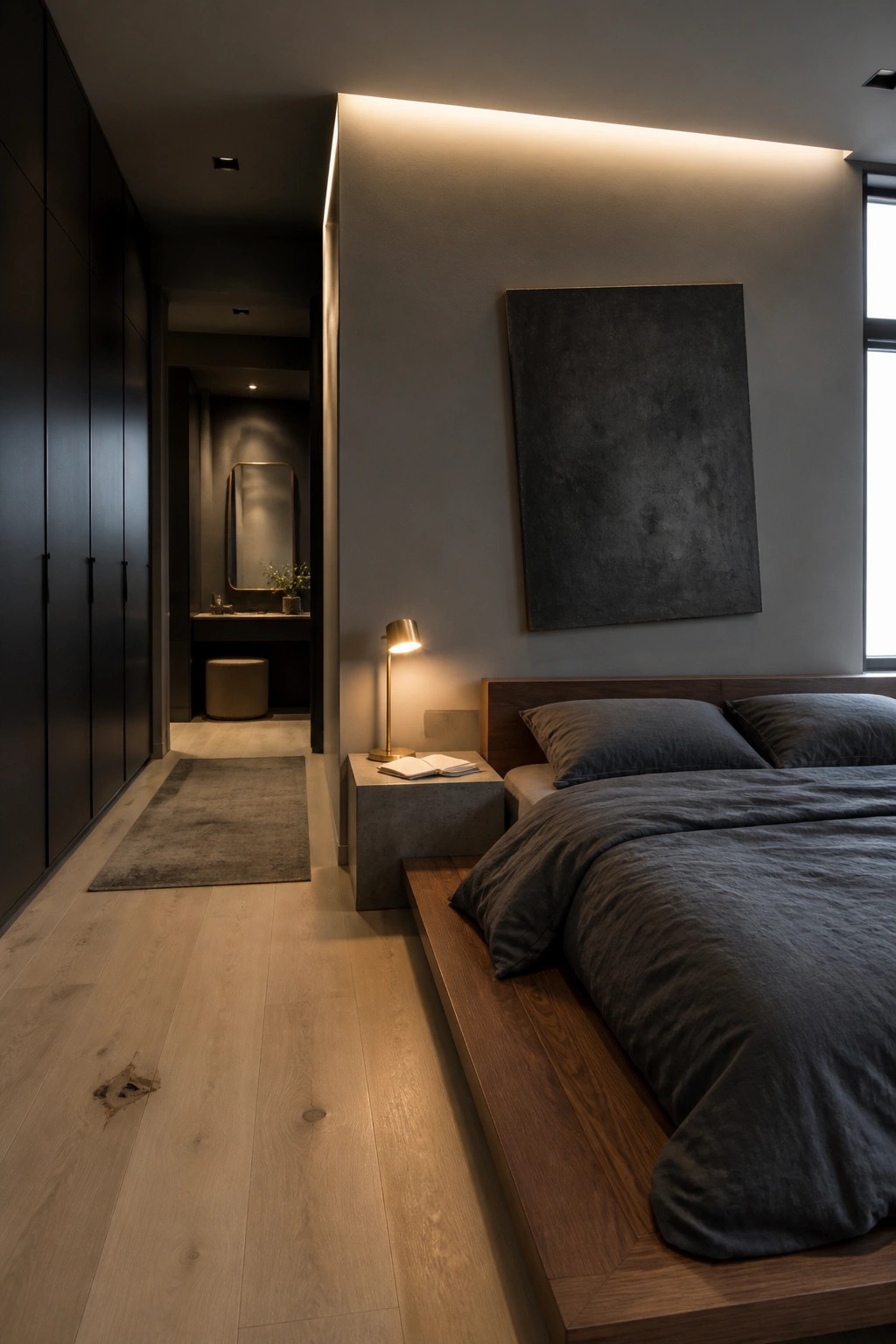 A modern bedroom with a low wooden platform bed covered in dark gray bedding, a concrete nightstand holding an open book and a small lamp, and a large dark abstract painting above the bed.