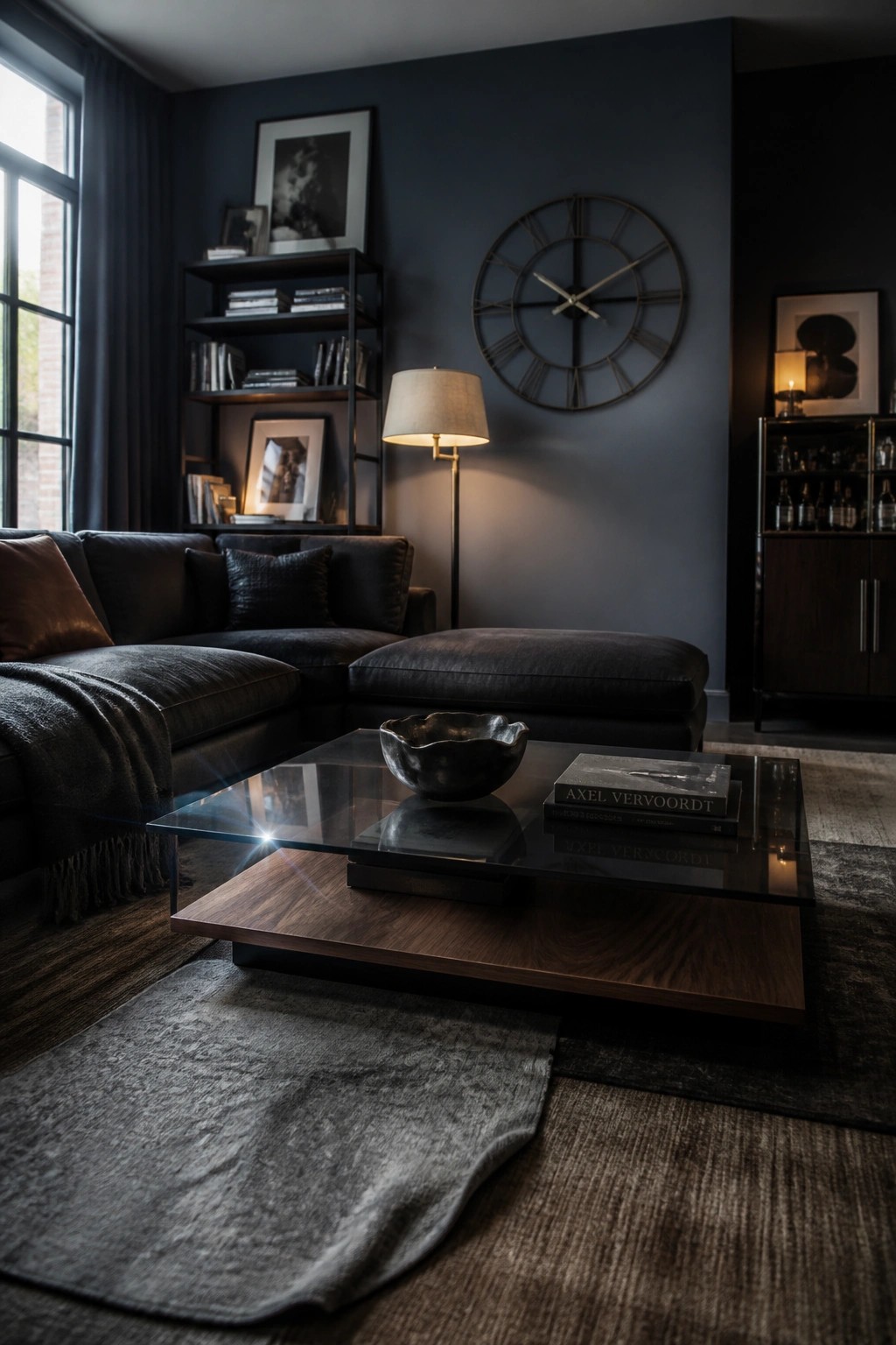 A modern living room with dark blue walls, a large dark sectional sofa, a glass-top coffee table with wood base, a floor lamp, and a large round wall clock.