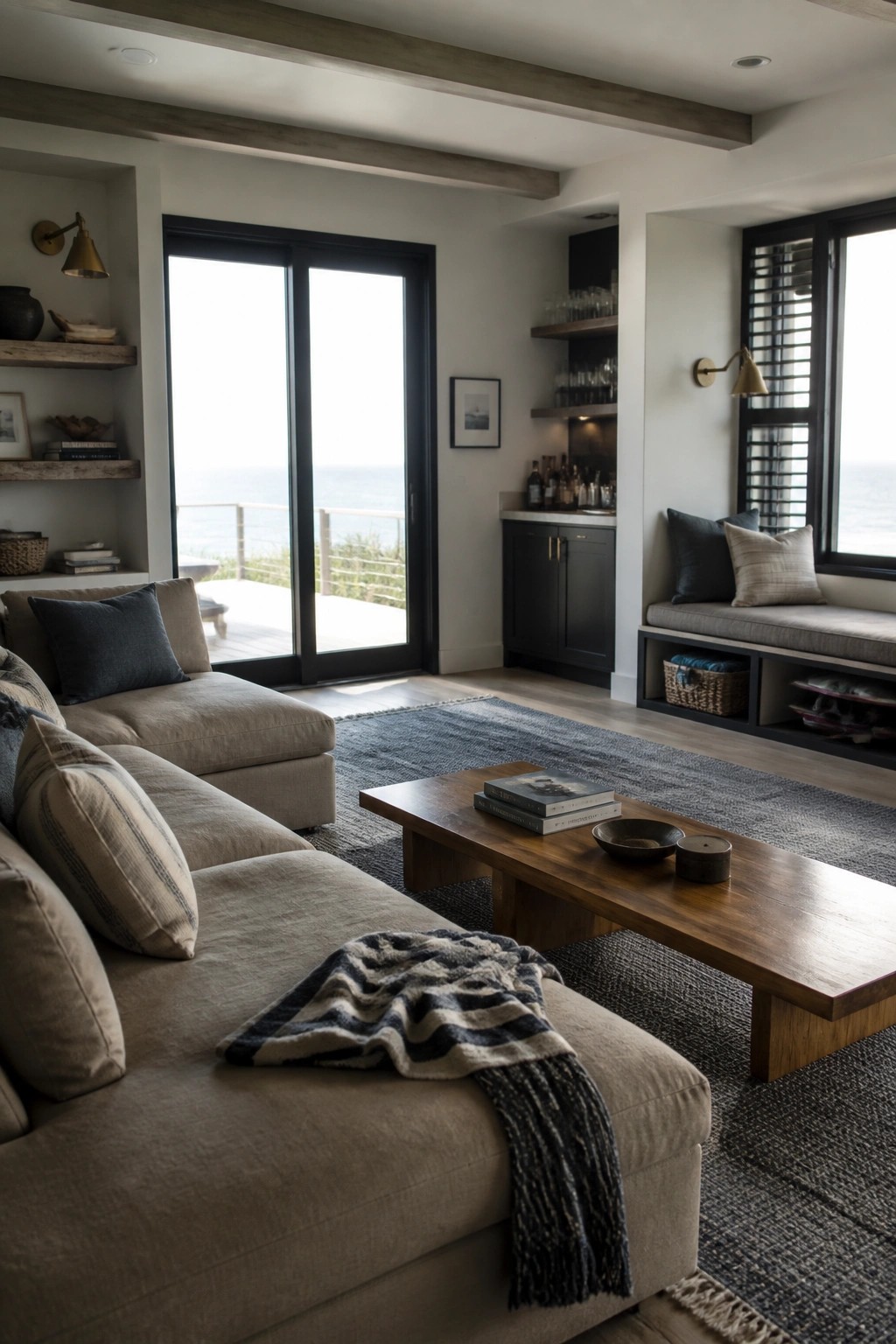 A living room featuring a large beige sectional sofa, wooden coffee table on a blue rug, built-in window seat, and glass doors with an ocean view.