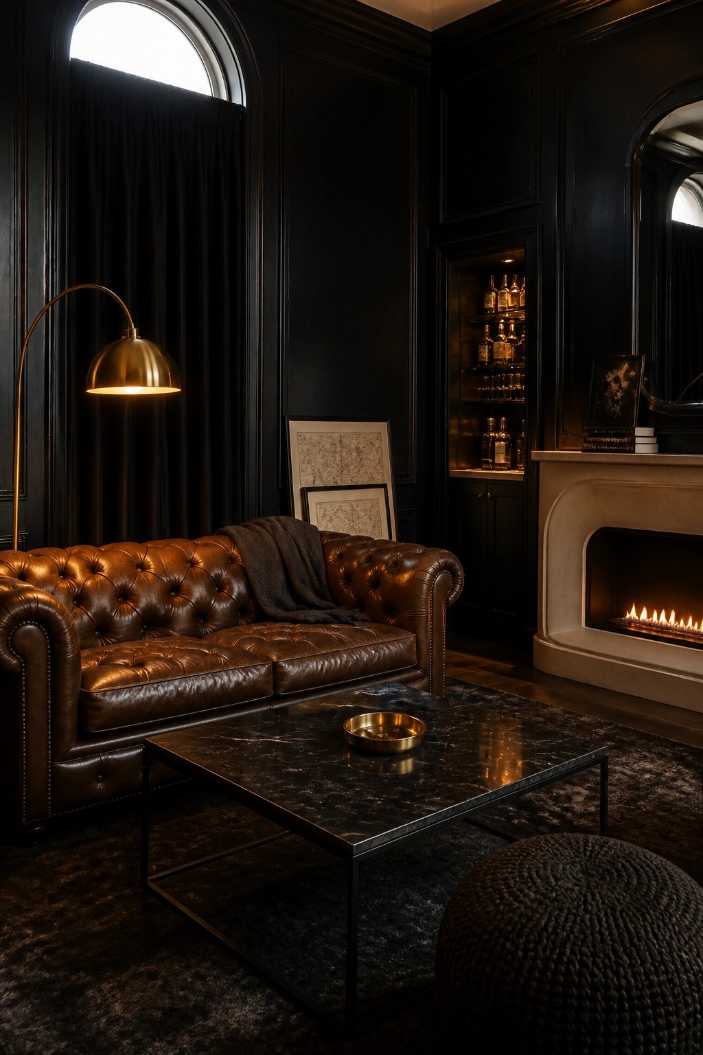 A living room with black paneled walls, a brown leather tufted sofa, a marble coffee table, and a lit fireplace.