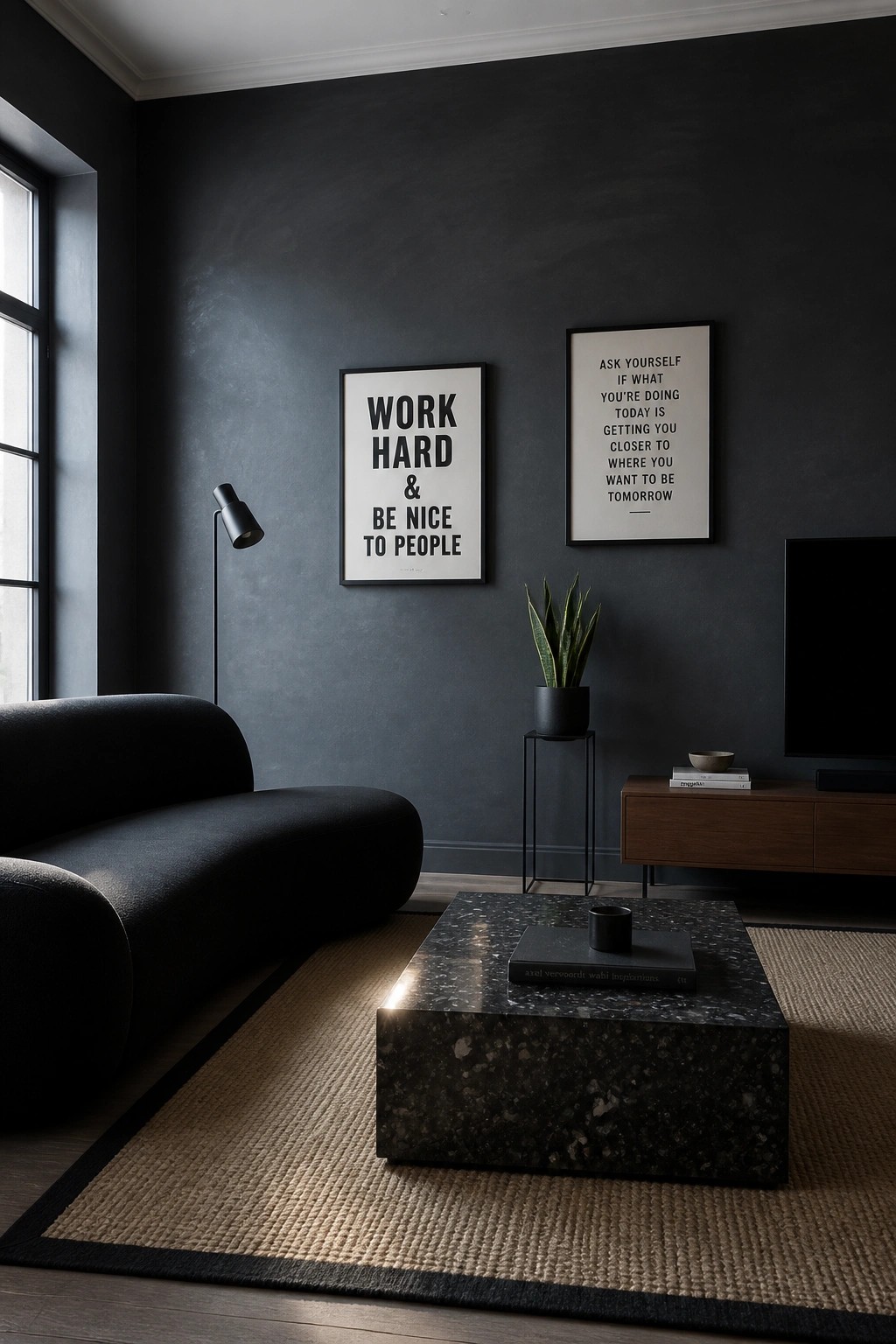A living room with dark gray walls, a black curved sofa, a black marble coffee table on a woven rug, two framed prints, a potted plant, and a wooden media console under a wall-mounted TV.