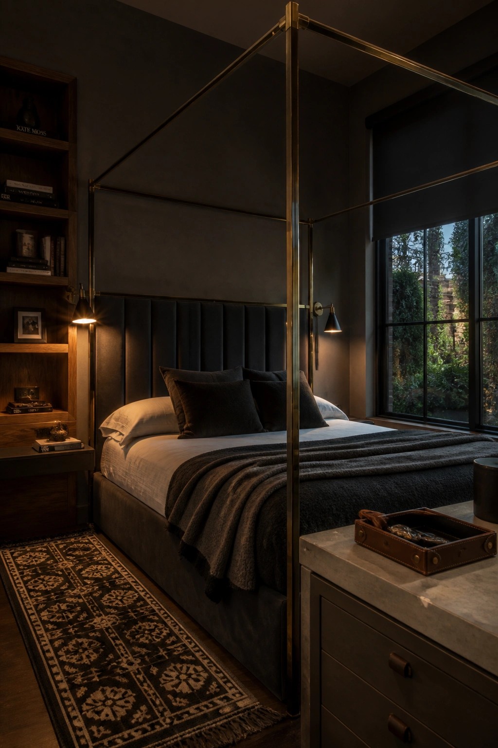 A bedroom with a brass four-poster bed frame, dark upholstered headboard, and built-in wooden bookshelves on the left wall.
