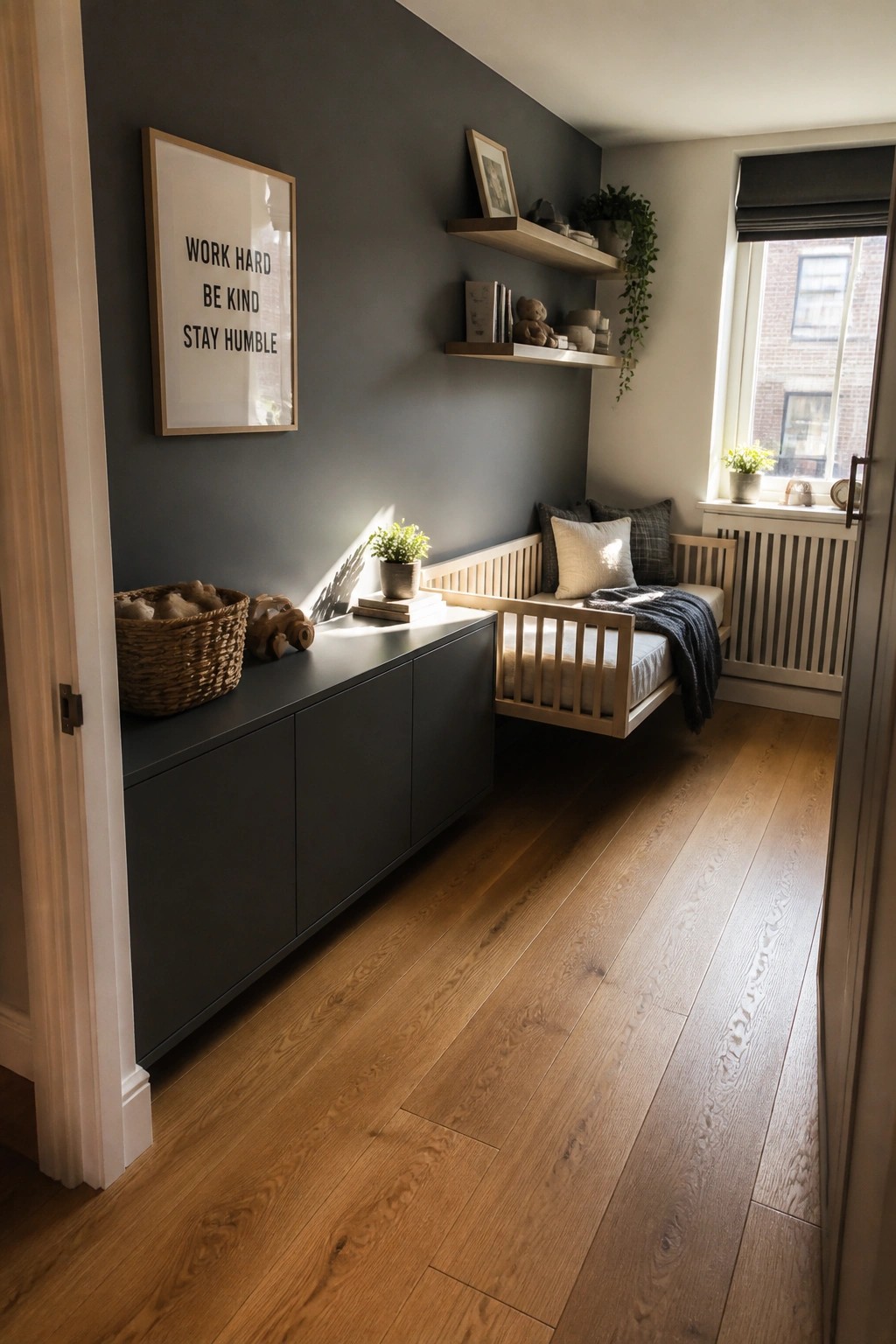 A narrow bedroom with dark walls shows a wall-mounted wooden bed, a long low cabinet, floating shelves, and an open wood floor walkway.