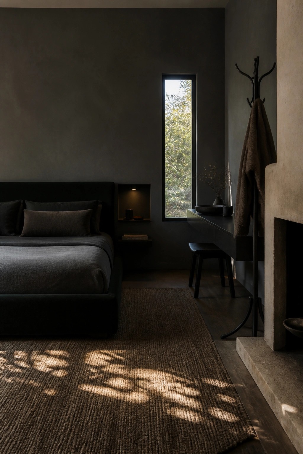 Dark minimalist bedroom with bed, tall window, desk, coat rack, and sunlit rug