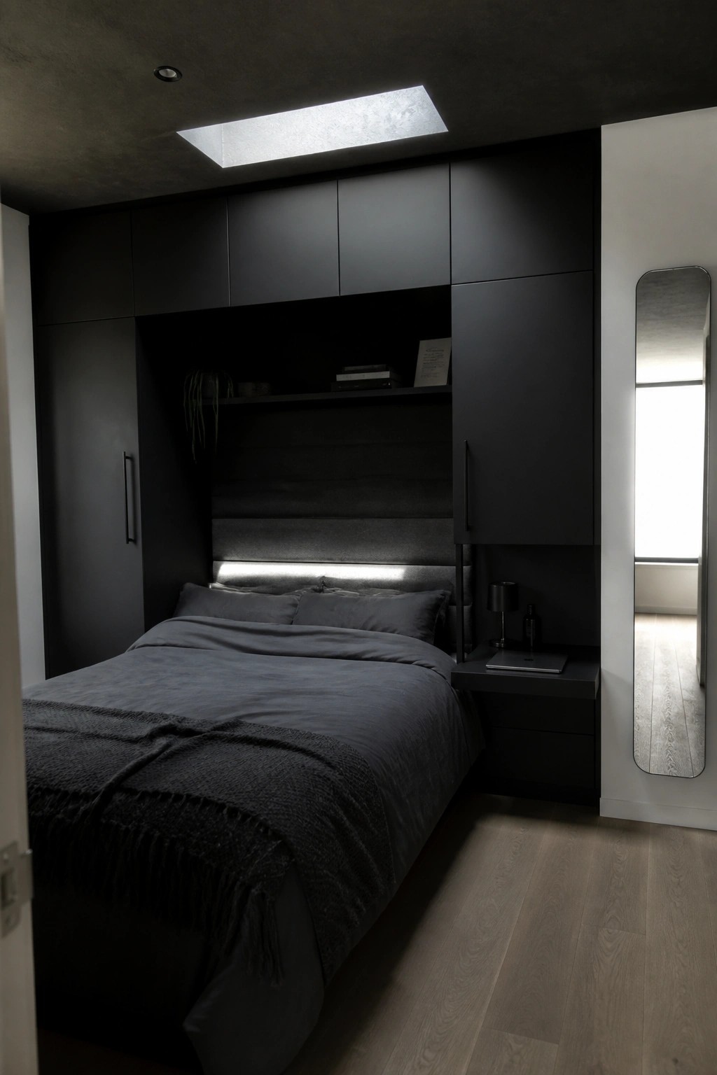 A small dark bedroom with built-in black cabinetry framing the bed, integrated headboard lighting, and a tall mirror on the right wall.