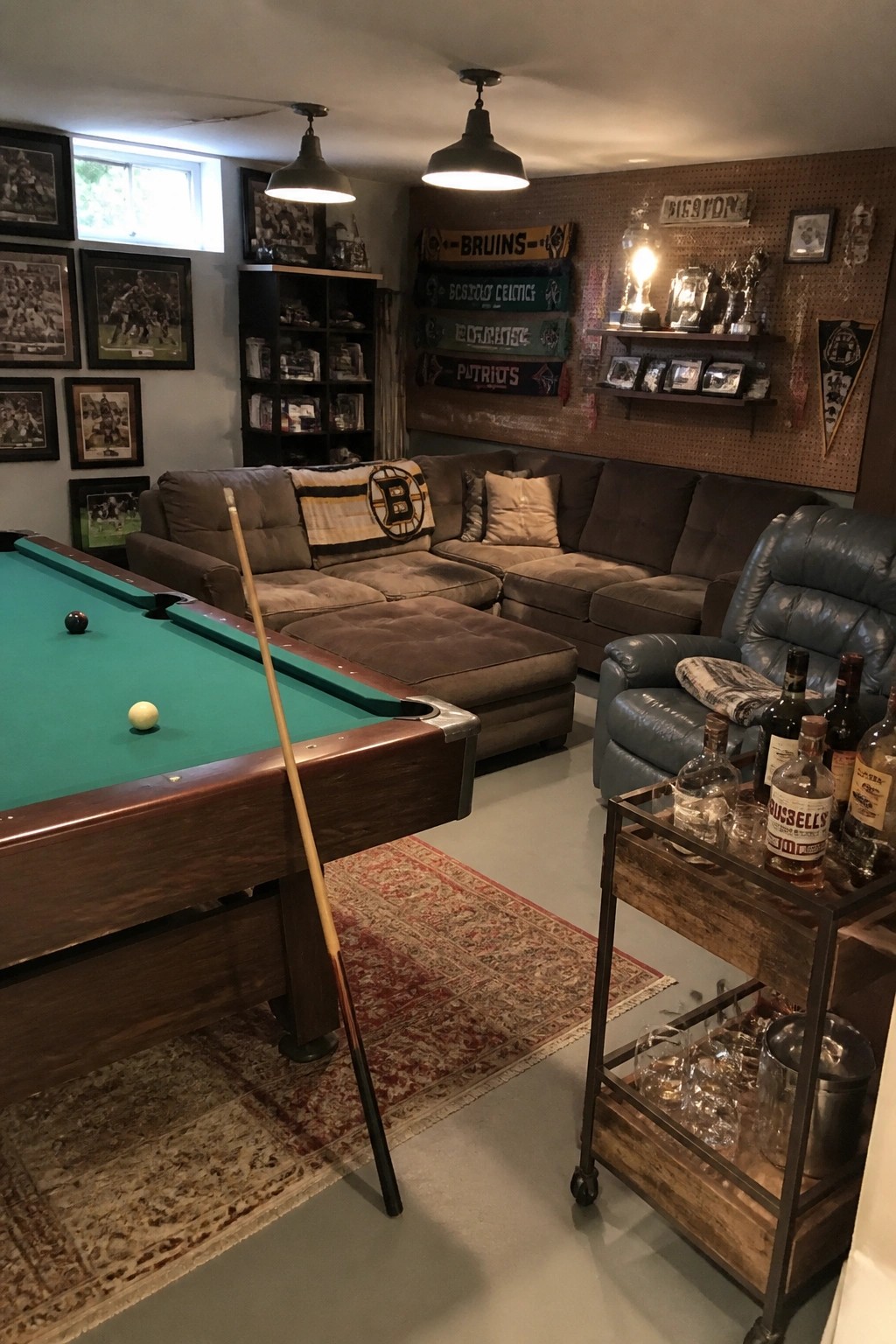 Basement rec room with pool table, brown sectional, blue recliner, and Boston sports banners.