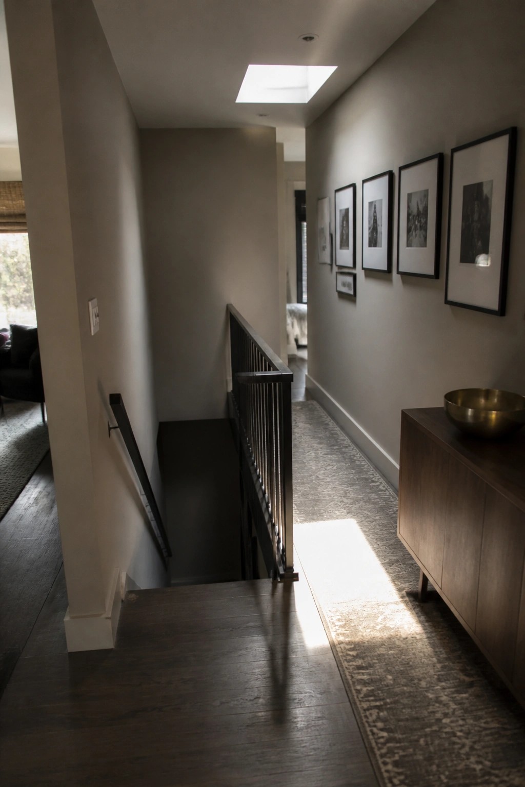 Modern hallway with dark wood stairs, black railing, framed art gallery wall, wooden console.