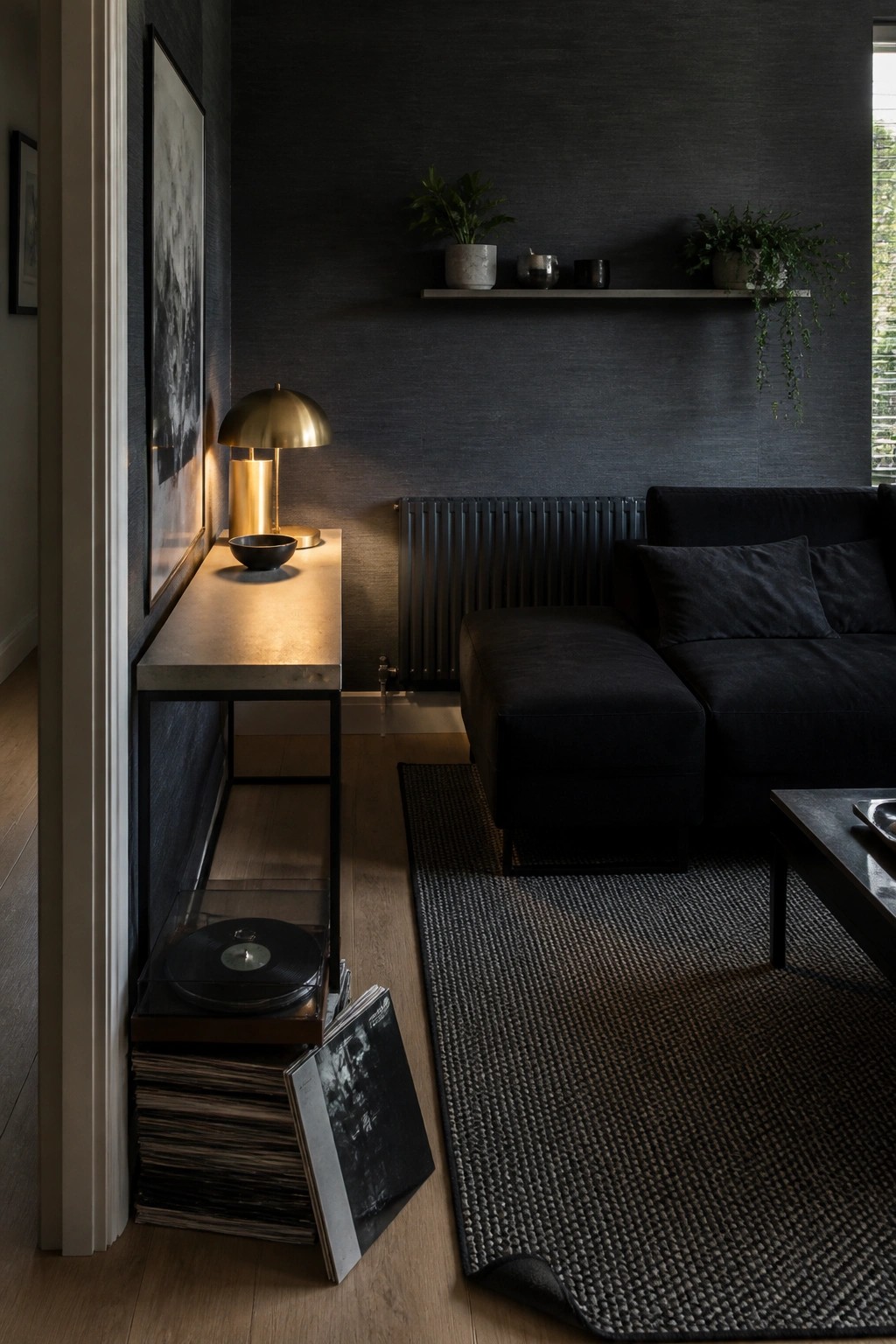 A dark masculine living room shows a narrow console table with a brass lamp and record player, plus vinyl records stored on a lower shelf and floor.