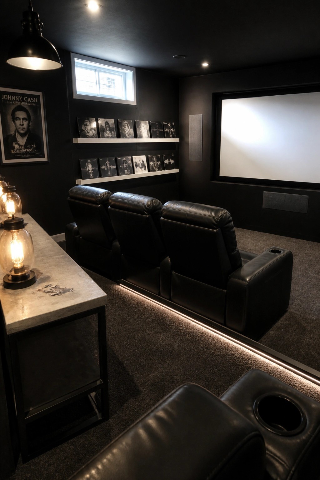 A dark home theater room with three black leather recliners, LED strip lighting along the base, and a large projection screen on the wall.
