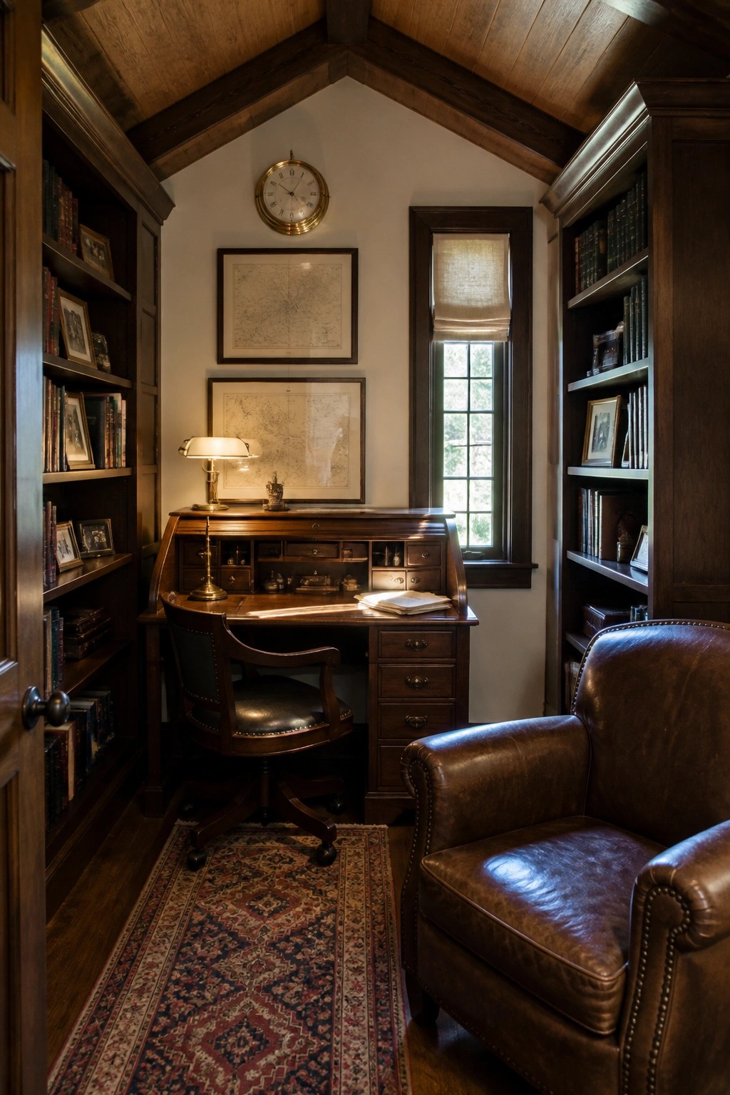 A traditional home office with dark wood built-in bookshelves on both sides of a roll-top desk, a leather swivel chair, a brown leather armchair, and framed maps on the wall.