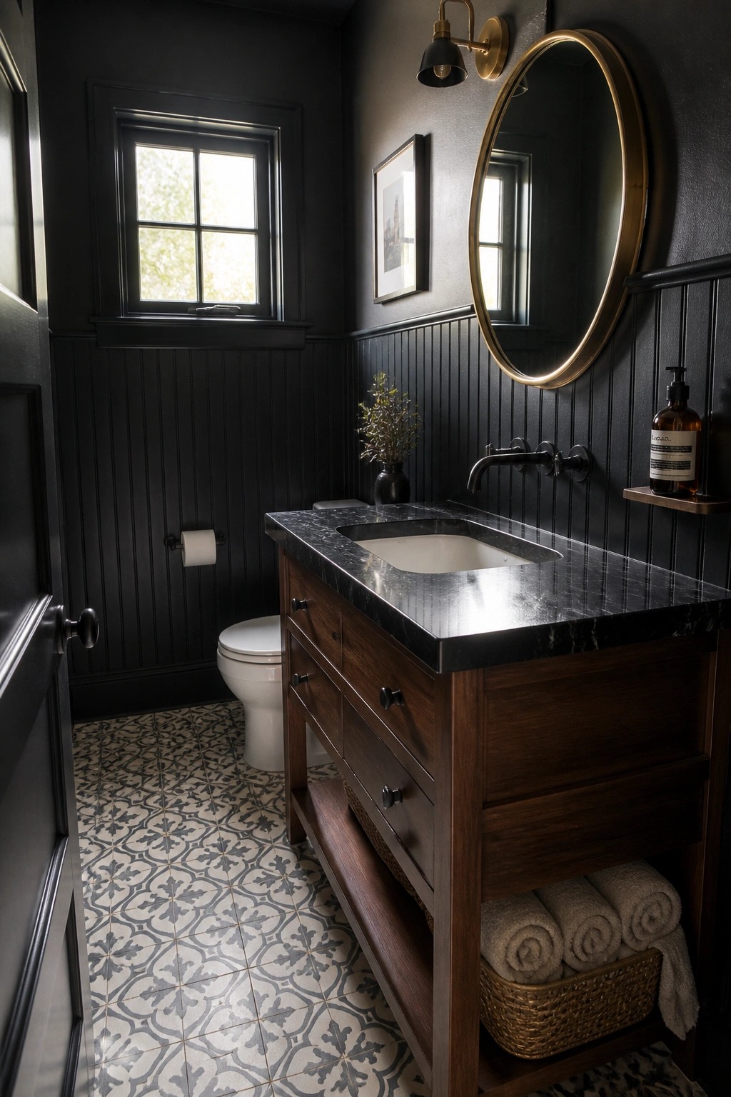Dark bathroom with wooden vanity, black marble sink, gold round mirror, and patterned floor.