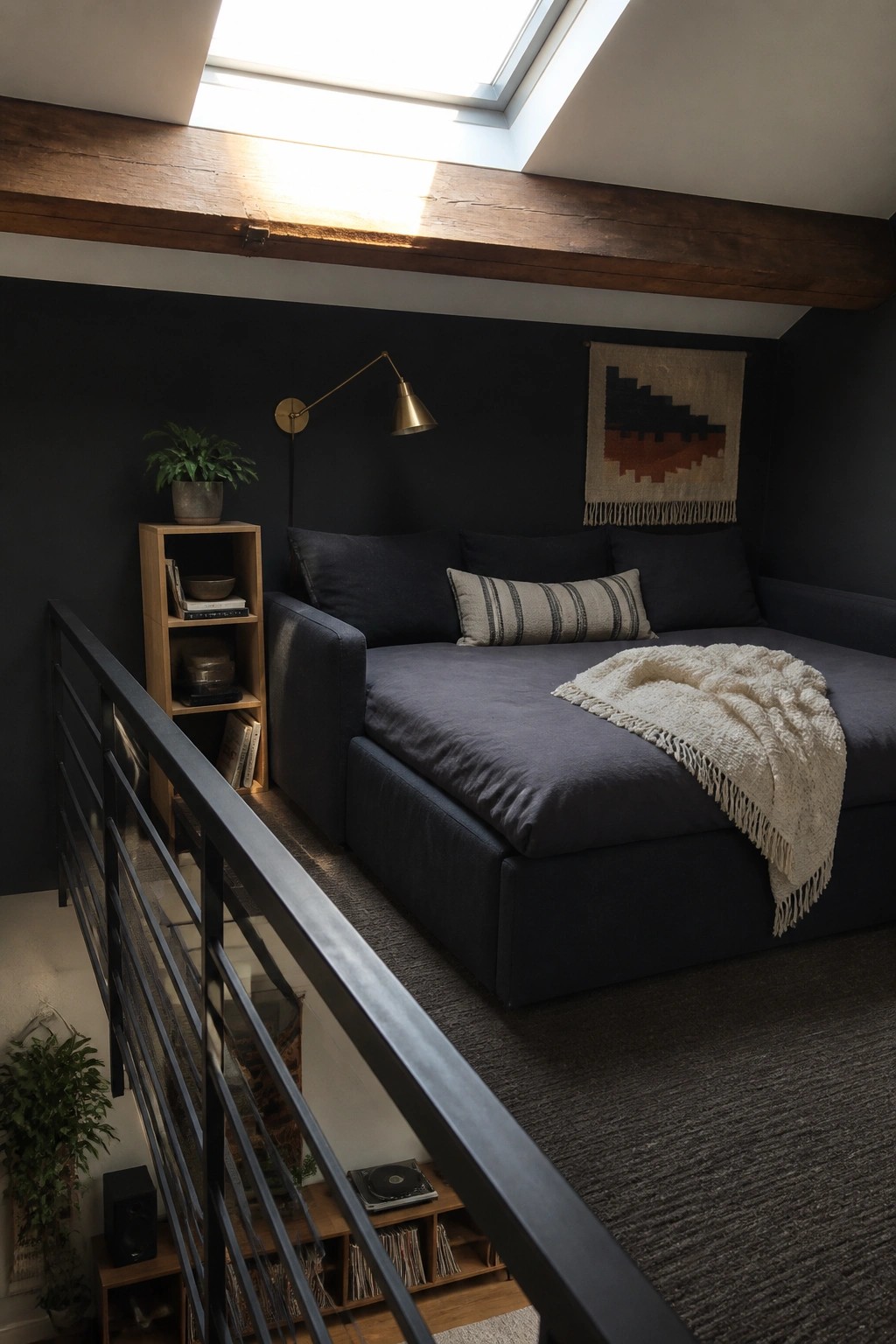 A bedroom with dark walls shows a large dark gray sectional sofa bed beneath exposed wooden beams and a skylight.