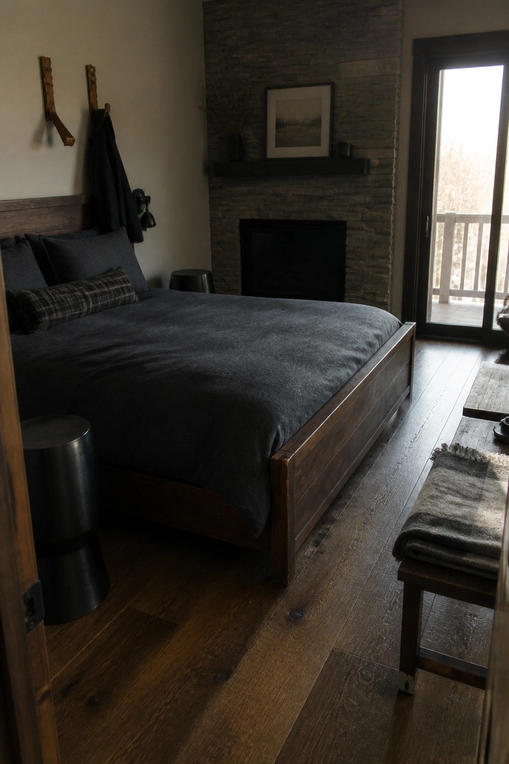 Rustic bedroom with dark wooden bed, gray bedding, stone fireplace, and bench.